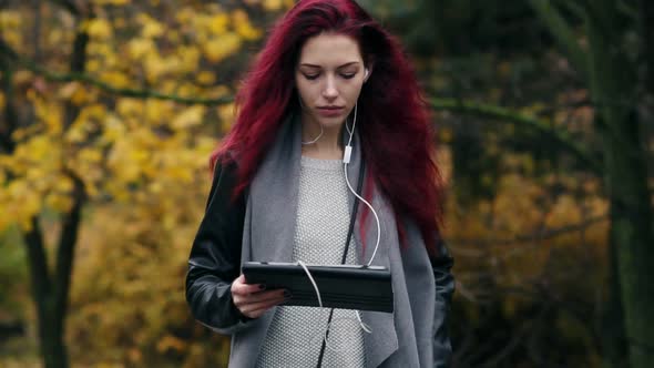 Young Businesswoman with Red Hair Walks in the Autumn Park and Communicates Via Tablet Pc