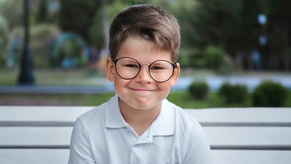 Portrait of Smiling Cute Boy Posing on Bench at City Park