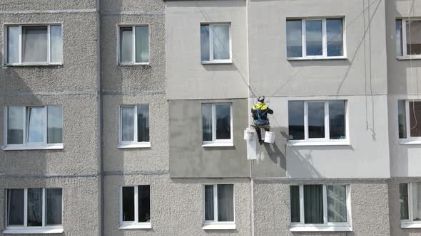 An Industrial Climber Suspended on Ropes and Paints the Wall of a Building with a Roller