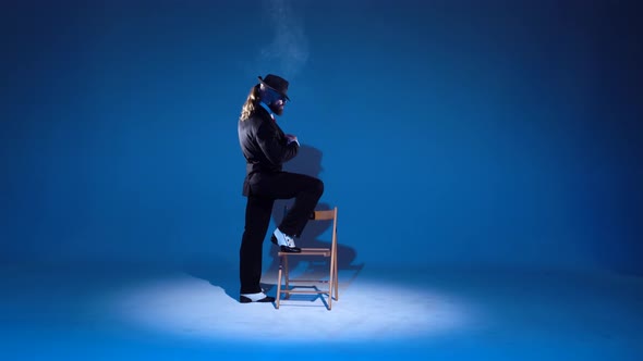 Elegant Man in a Black Hat Is Dancing an Erotic Dance, Spotlight on a Blue Background