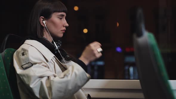 Young Stylish Woman Wearing on Wireless Headphones and Listening To Music on Mobile Phone in Public