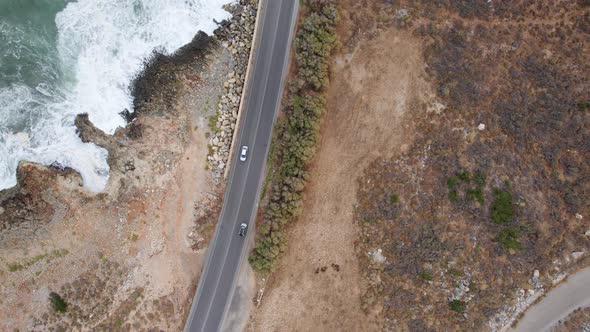 Following cars Aerial top down view from above on the country road between rocks and ocean waves