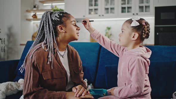 Cute Little Black Girl Playing Beauty Salon Game with Her Pretty Mother Applying Eyeshadows on Mommy