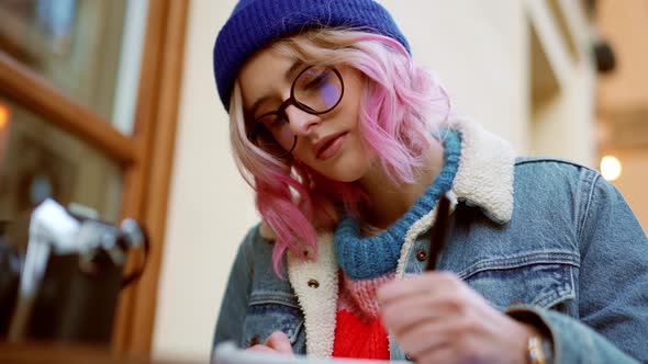 Pensive woman in hat drawing something in cafe