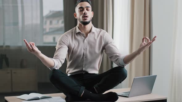 Mindful Calm Arabian Business Man Employee in Lotus Position Sit on Work Desk Closed Eyes Meditating