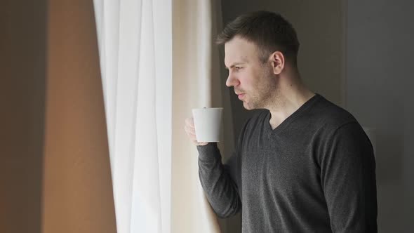 Young 30s Man Looking Out Window Enjoying New Day with Cup of Tea or Coffee