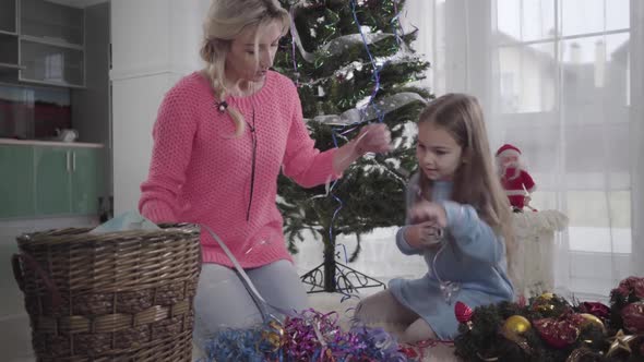 Brunette Caucasian Girl Choosing Garlands with Mom As Sitting at the Background of New Year Tree