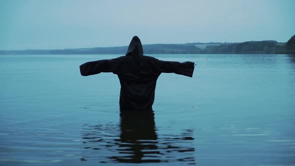 Female figure in a black robe in the river. Divination in the night of Halloween.