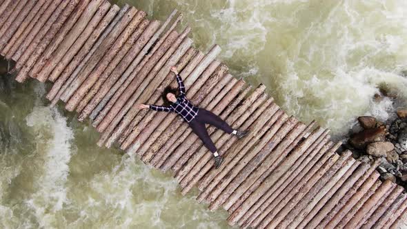 Young Woman Lies on Wooden Footbridge Over Rough River