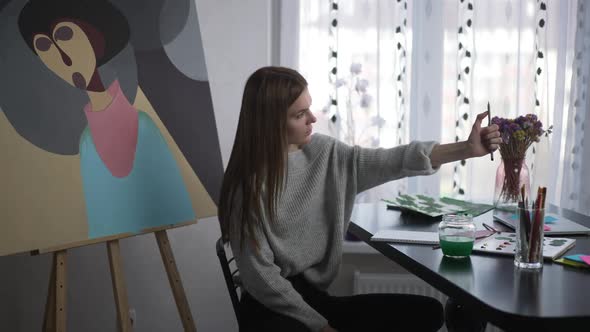 Concentrated Young Woman Stretching Hand Looking at Pencil Drawing Sketch on Paper