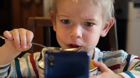 Little Boy Using Phone While Eating Soup During Lunch or Dinner