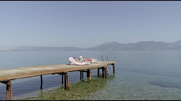 Aerial view passing by two attractive woman sunbathing in Panagopoula, Greece.