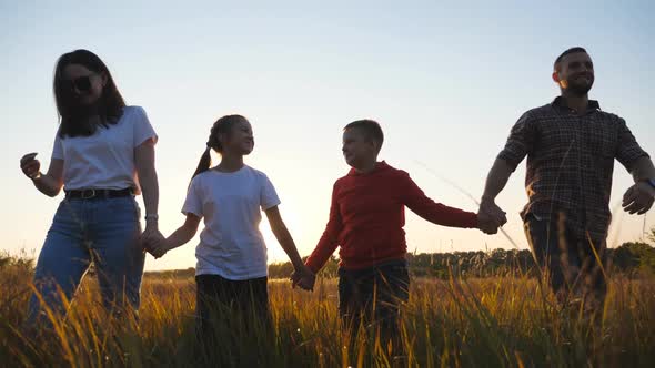 Happy Parents with Small Kids Walk Through Grass Field Holding Hands of Each Other at Sunset