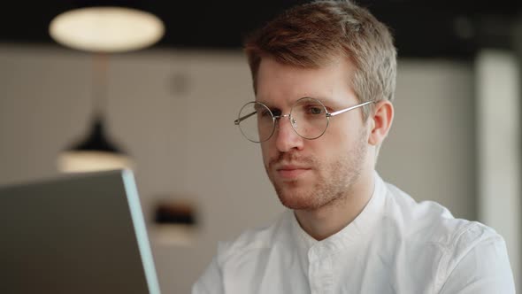 Male Student with Glasses is Reading Info on Laptop Display Learning Online Technology for Distant