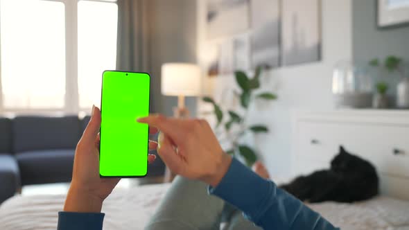 Woman at Home Lying on a Bed with Black Cat and Using Smartphone with Green Mockup Screen in