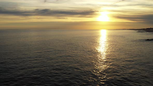 Pull away over surfers in the Atlantic Ocean during a golden sunset then rise up as the camera pulls