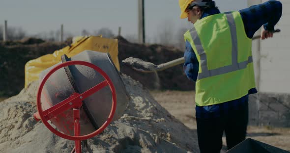 Male Construction Worker Putting Cement in Mixer with Shovel