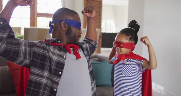 Happy african american daughter and father having fun, wearing superhero costumes
