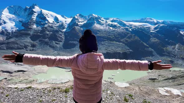 Back View of a Young Girl Embracing Fresh Air with Mountains Covered By Snow in Summer Season