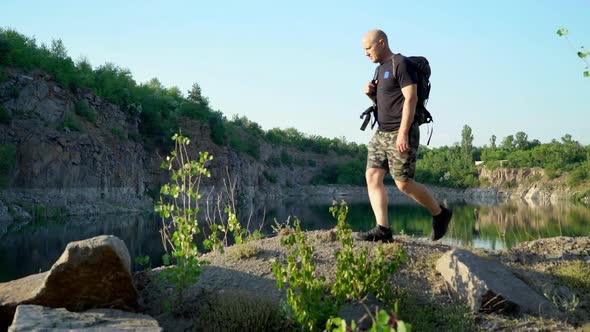 Traveler in sportswear and with a backpack walks along the quarry above the lake