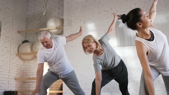Mature Man and Woman Doing Yoga with Teacher in Studio