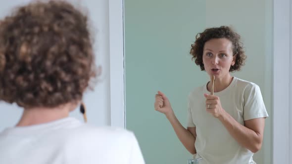A Wellgroomed Young Woman in Front of the Mirror Holding a Toothbrush Dances and Sings