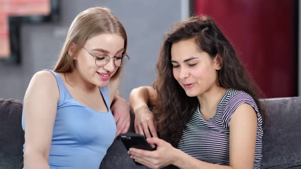 Young Happy Blonde and Brunette Woman Talking Looking at Screen of Smartphone Enjoying Friendship