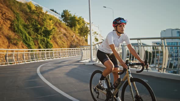 Sportswoman in Protective Helmet is Riding Trekking Bike Downhill Along Bridge Surrounded By Modern