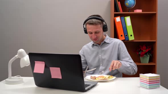 Young Office Worker Student Manager Wearing Headphones Eating His Lunch in His Home Office During a