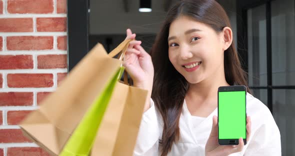 Attractive young woman holding smart phone with green screen and shopping bags.