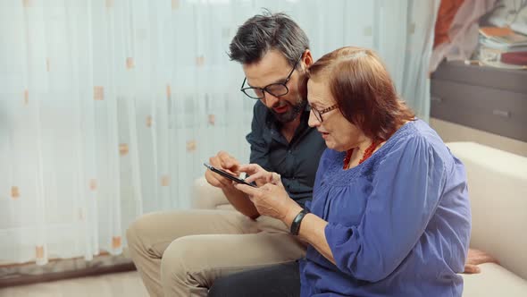 Old Granny With Grandson Looking On Smartphone. Grandson Teaching Grandma Using Mobile Phone.