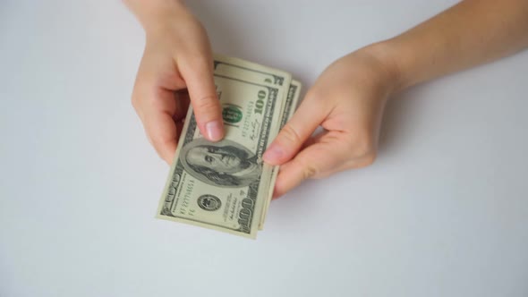 A Woman Counts Dollar Bills for 100 Dollars on a White Background Top View