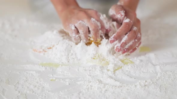 Close up of hands kneading dough in flour and eggs on the table with for making various desserts.