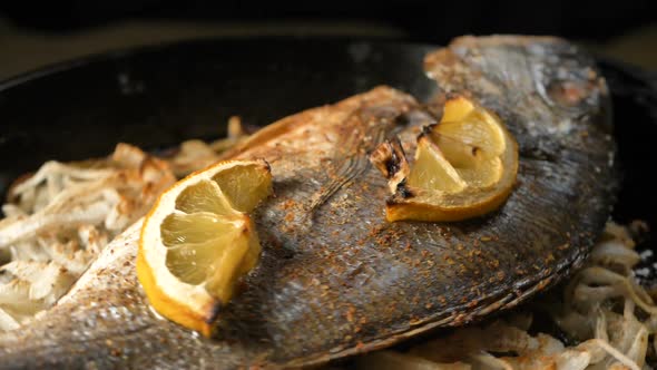 Pan with Fried Dorada Fish on Onion Slices and Lemon on Top