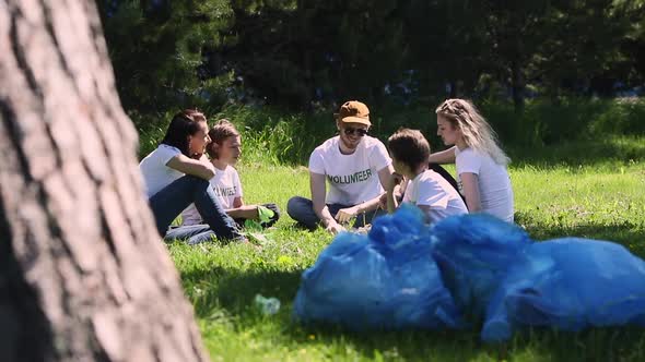 Volunteer Family Recycle Plastic Bottle Group Gathering in Park and Discussing Cleaning Plan Spbi