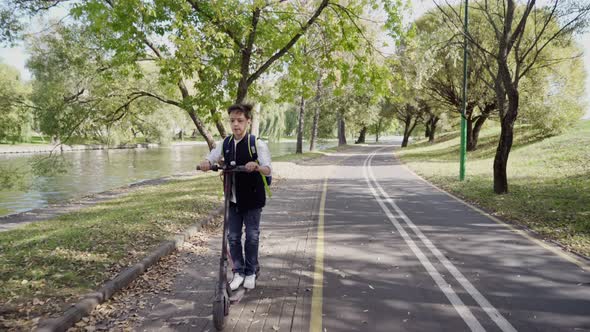 School Boy Riding with His Electric Scooter in the City with Backpack on Sunny Day