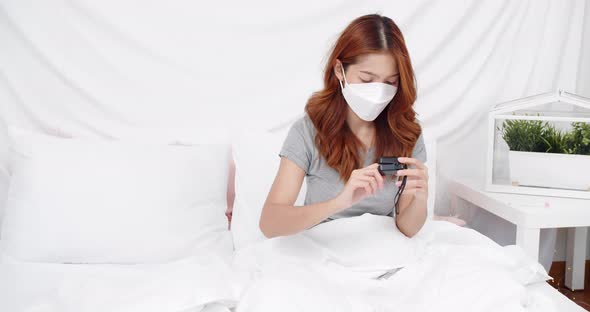 Asian woman with mask measuring blood oxygen saturation level with pulse oximeter at home during the