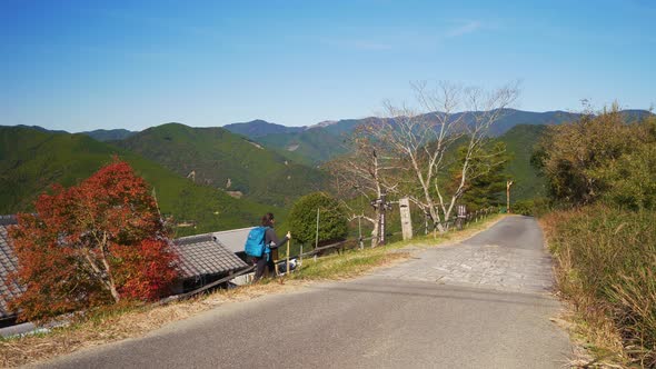 Static, female walks path through village in lush mountain landscape , Japan