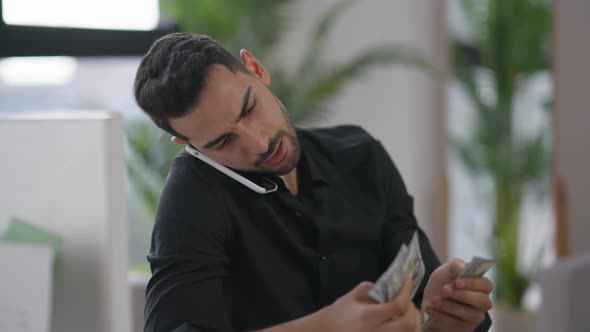Wealthy Young Middle Eastern Businessman Talking on Smartphone Counting Money