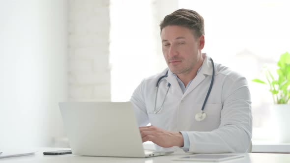 Male Doctor Showing Thumbs Up Sign While using Laptop in Office