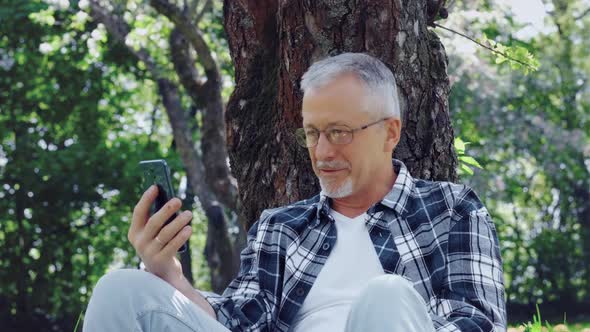 An Elderly Whitehaired Man with Glasses Talks on the Phone and Enjoys the Fresh Air and Nature