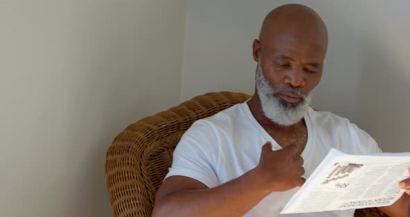 Front view of black mature man reading newspaper at home 4k