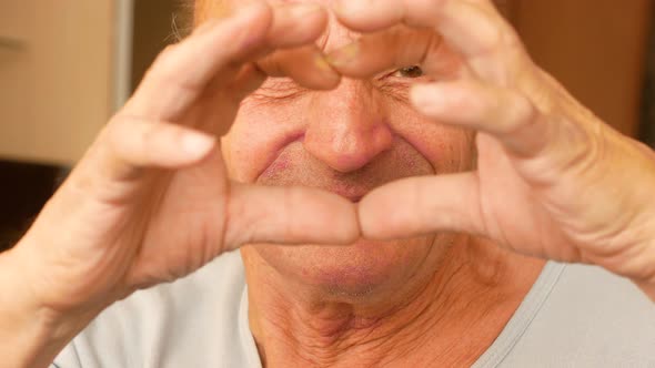 portrait of caucasian cheerful smiling elderly man over 70 showing hands gesture of love.