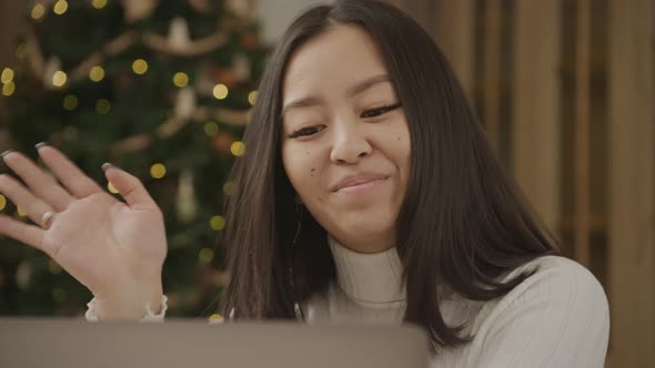 Close Up Asian Woman on a Video Call on Her Laptop with a Christmass Tree on Background Indoors