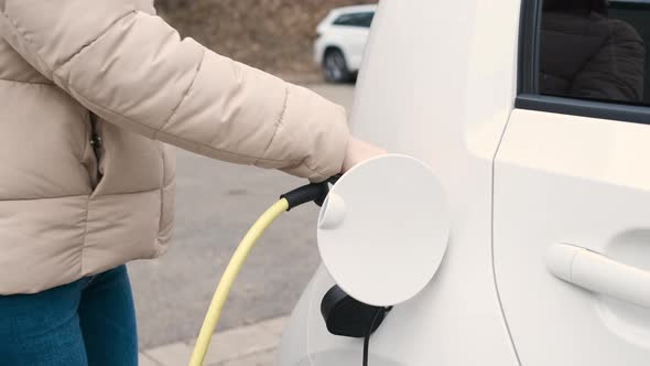 Woman Coming to the Electric Vehicle and Unplugging Power Supply Cable to Charge in the Street at