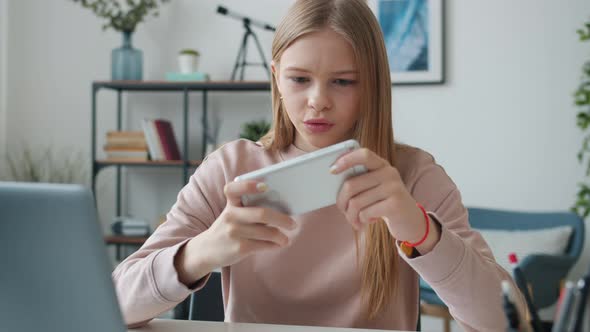 Joyful Girl Having Fun Playing Video Game with Smartphone Relaxing at Home in Leisure Time
