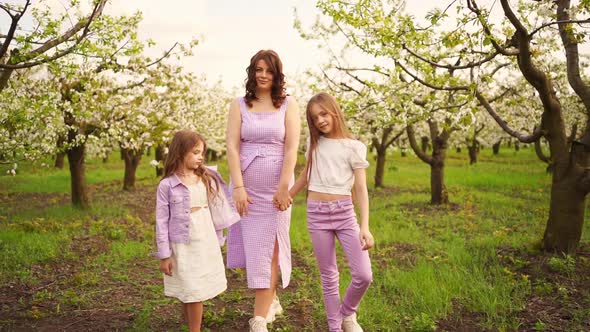 Mom Walks and Holds Hands Her Daughters in the Garden Among the Flowering Trees