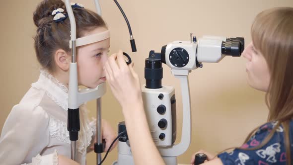 Woman Eye Doctor Is Correcting Head of Little Girl Near Biomicroscopy Apparatus