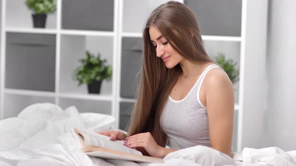 Domestic Beautiful Girl Enjoying Leisure Reading Book Sitting on Bed