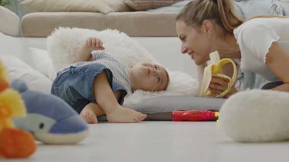 Happy and smiling mom makes your beautiful child baby eat banana